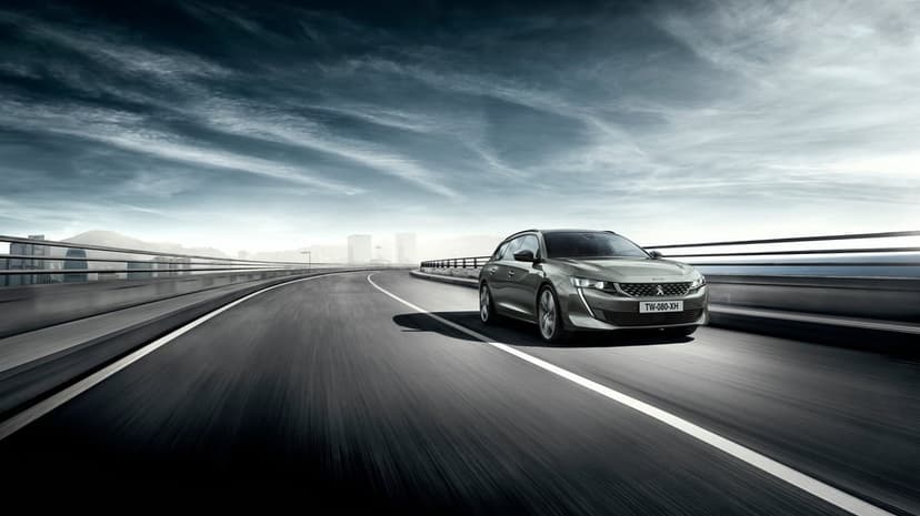 Gray Peugeot 508 SW driving on a curved highway bridge with motion blur under a dramatic desaturated sky.