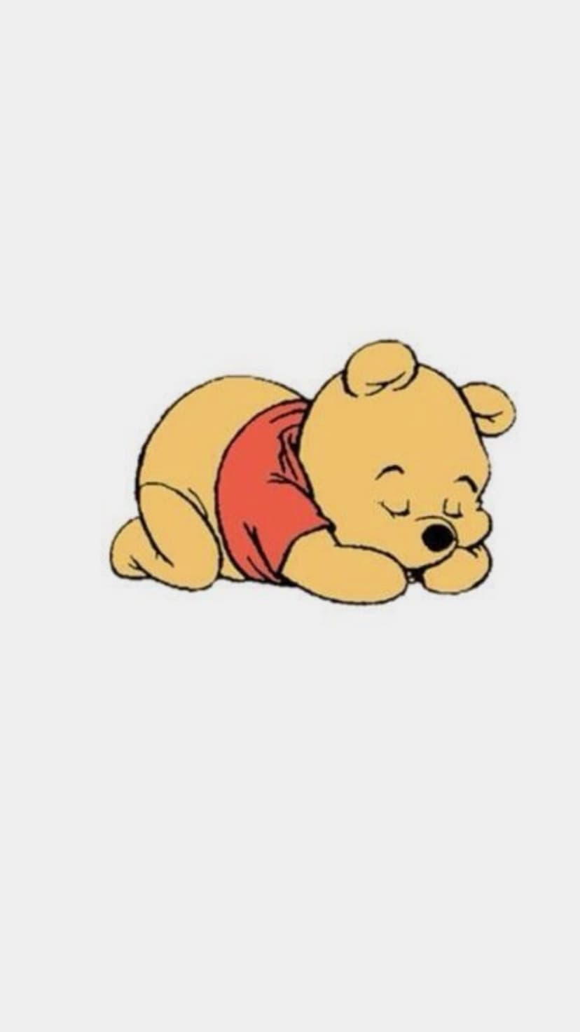 Winnie the Pooh sleeps in a red shirt while curled up against a solid white background with paws tucked inward.