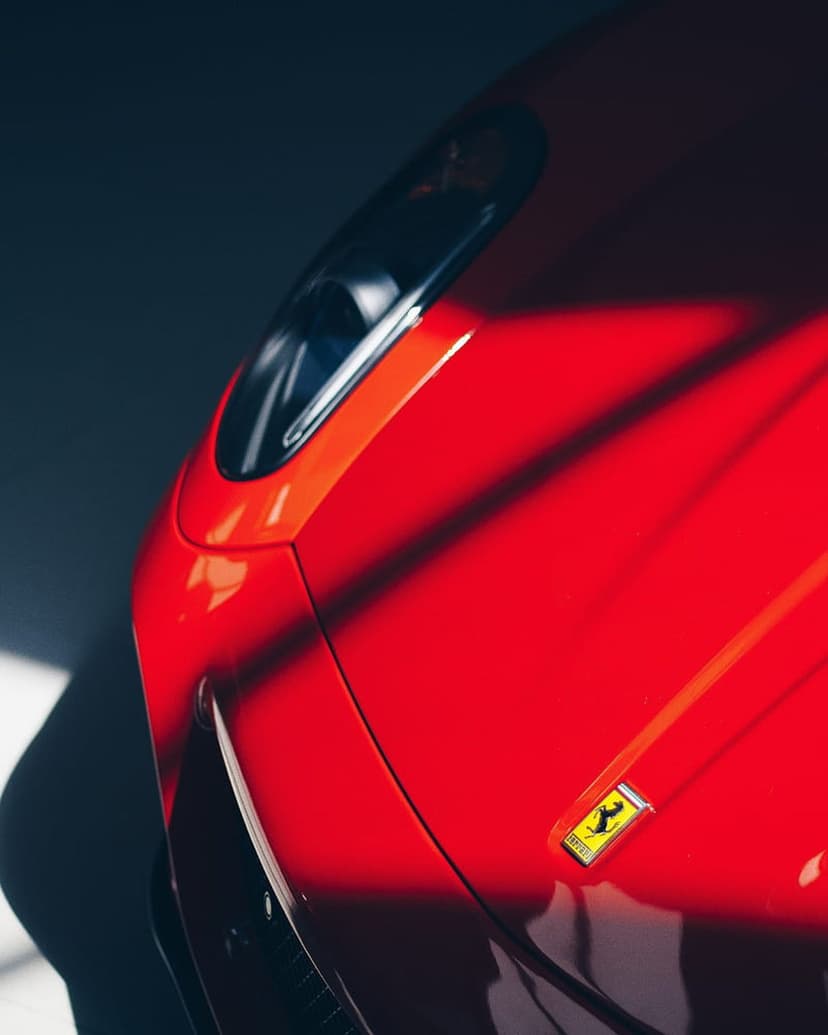 Ferrari badge rests on a red hood defined by dramatic diagonal shadows and sharp highlights in close-up.