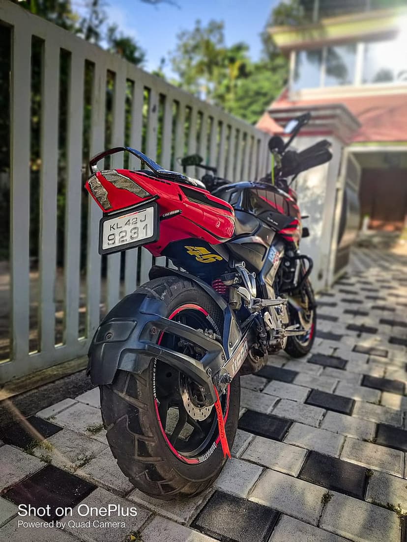 Red and black sportbike rear view with a visible license plate on patterned pavement under dappled sunlight.