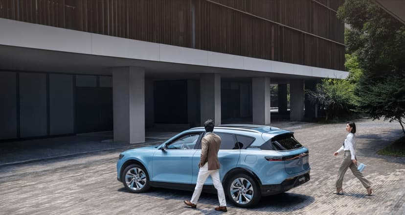 Light blue luxury SUV parked in a modern stone courtyard with two people walking near it by a slatted building.
