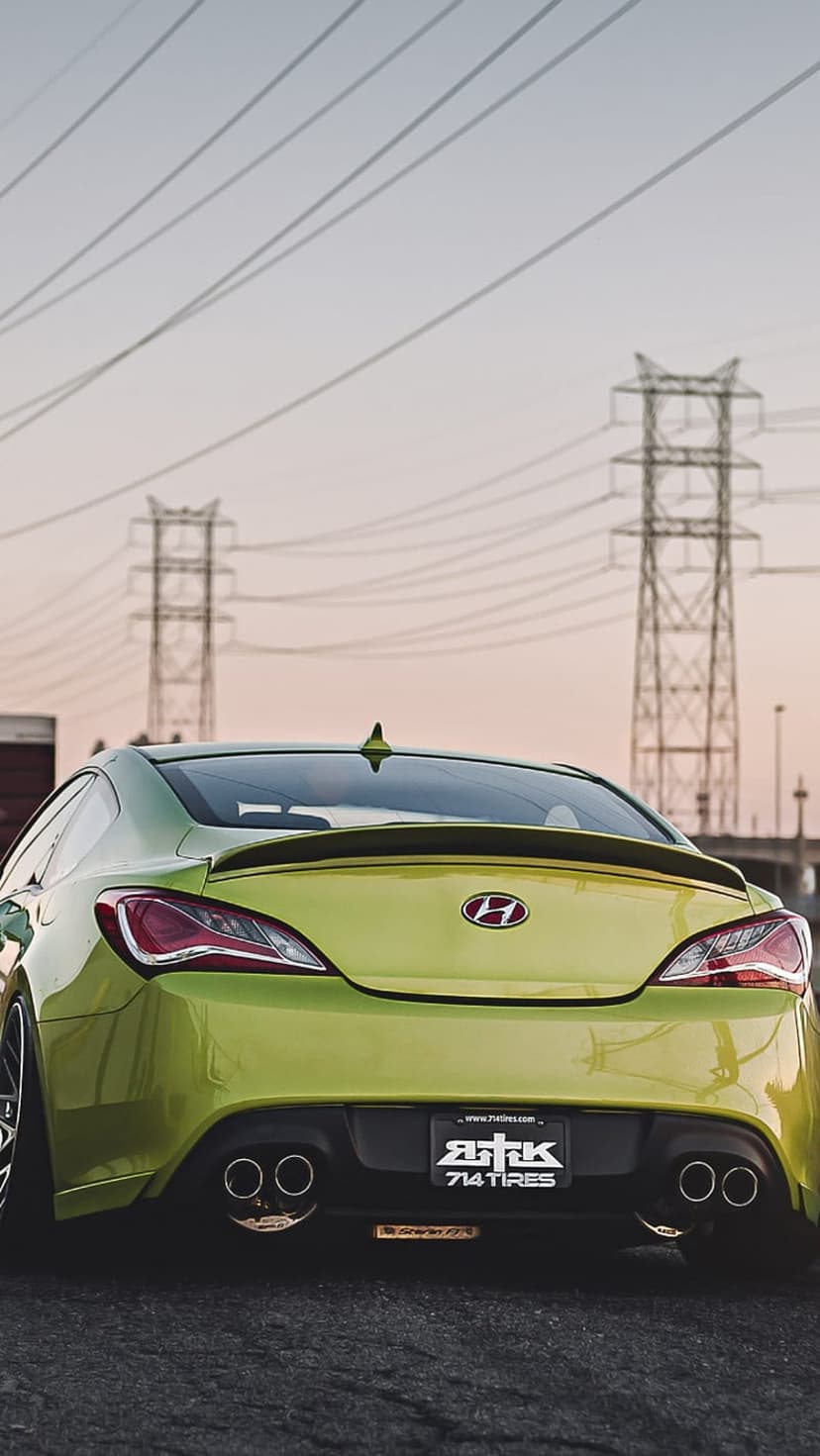 Lime green Hyundai Genesis Coupe rear view showing dual exhausts and spoiler on asphalt under a dusk sky.