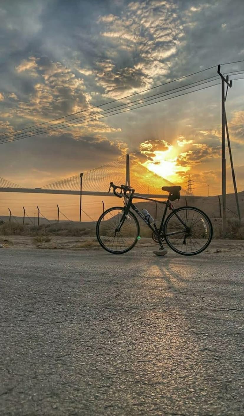 Road bike silhouette on a rural asphalt road during a vibrant golden sunset with dramatic clouds and utility poles.