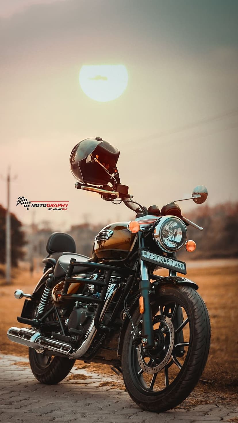 Royal Enfield motorcycle in gold with a black helmet on the handlebars during a warm sunset on a gravel path.