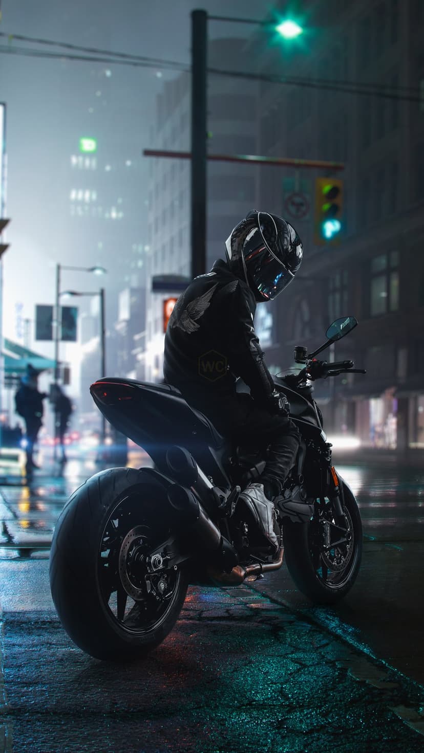 Motorcyclist in black gear sits on a bike on a wet street with vibrant neon reflections at night.