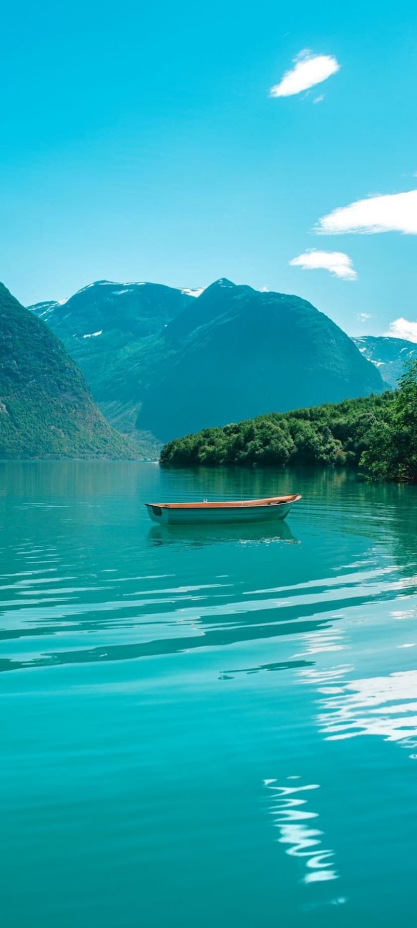 Solitary orange boat on turquoise water between steep green mountains with snow peaks under a blue sky.