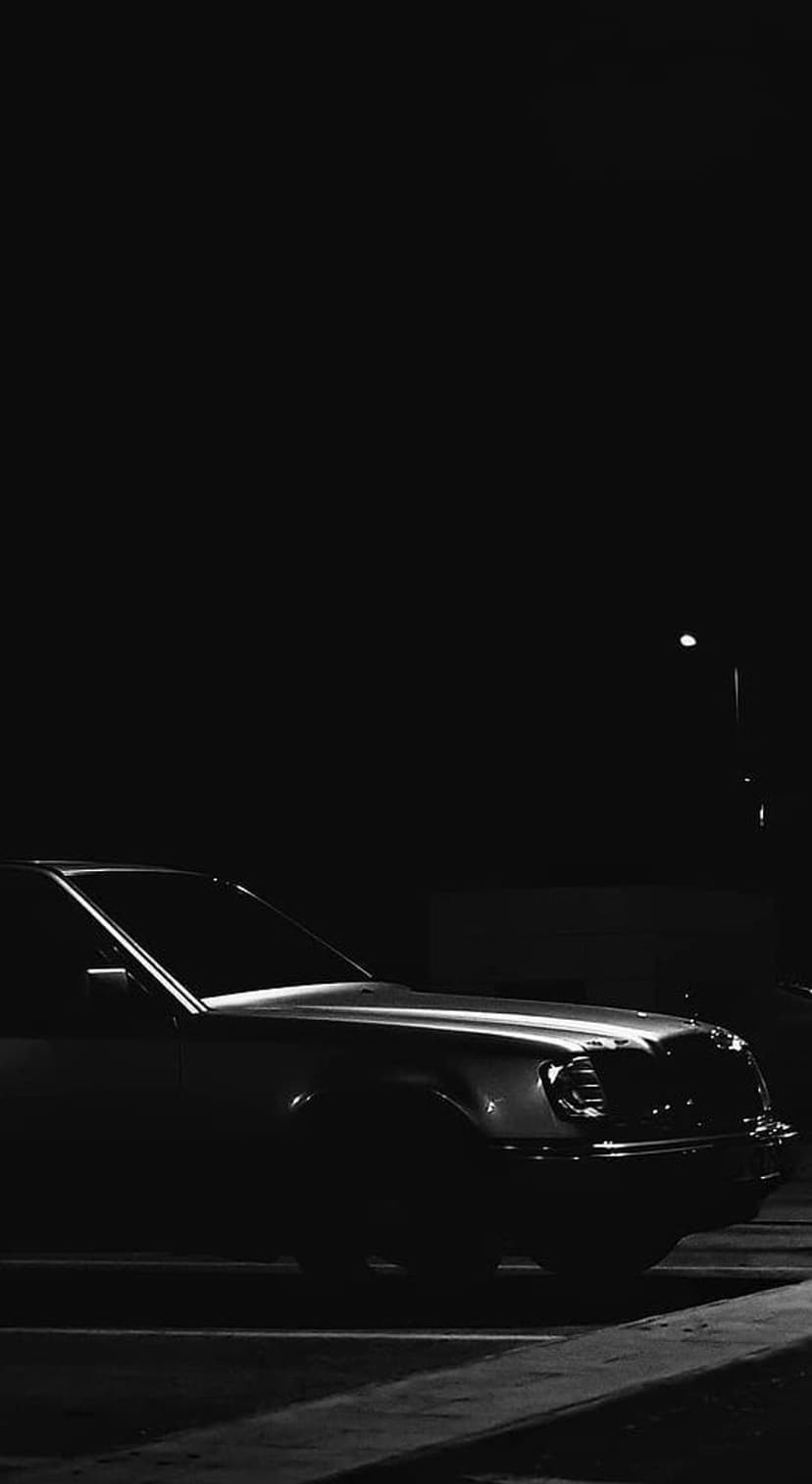 Vintage Mercedes-Benz sedan parked under a streetlamp at night in a high-contrast black and white photograph.