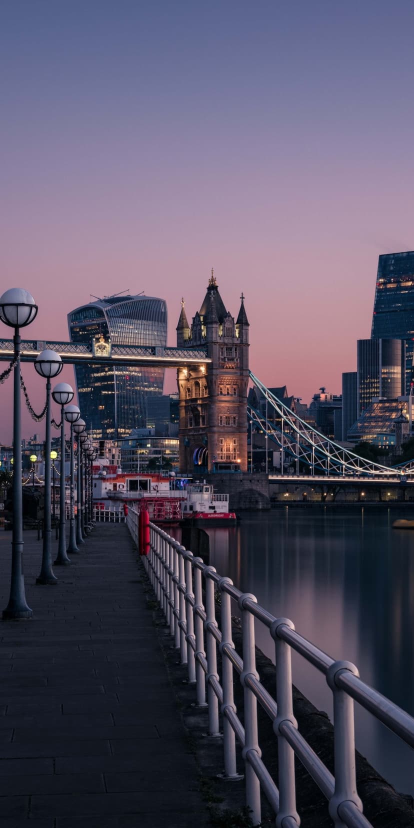 Tower Bridge illuminated at dusk with blue and orange sky reflections on the River Thames water surface.