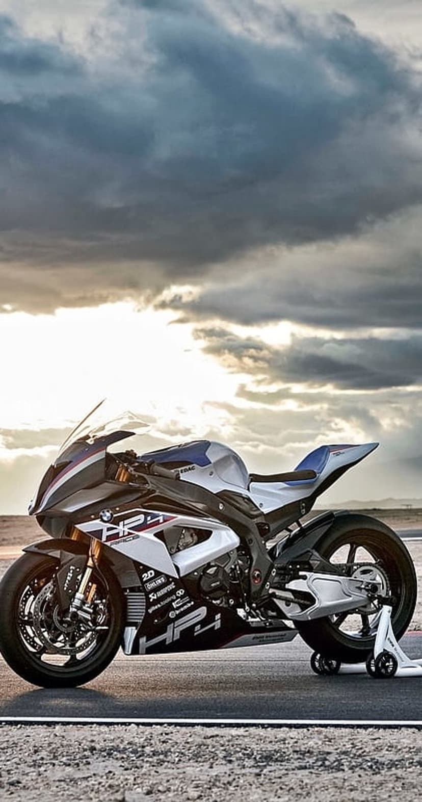 BMW HP4 motorcycle on a race track asphalt under a dramatic sunset sky with orange and blue clouds.