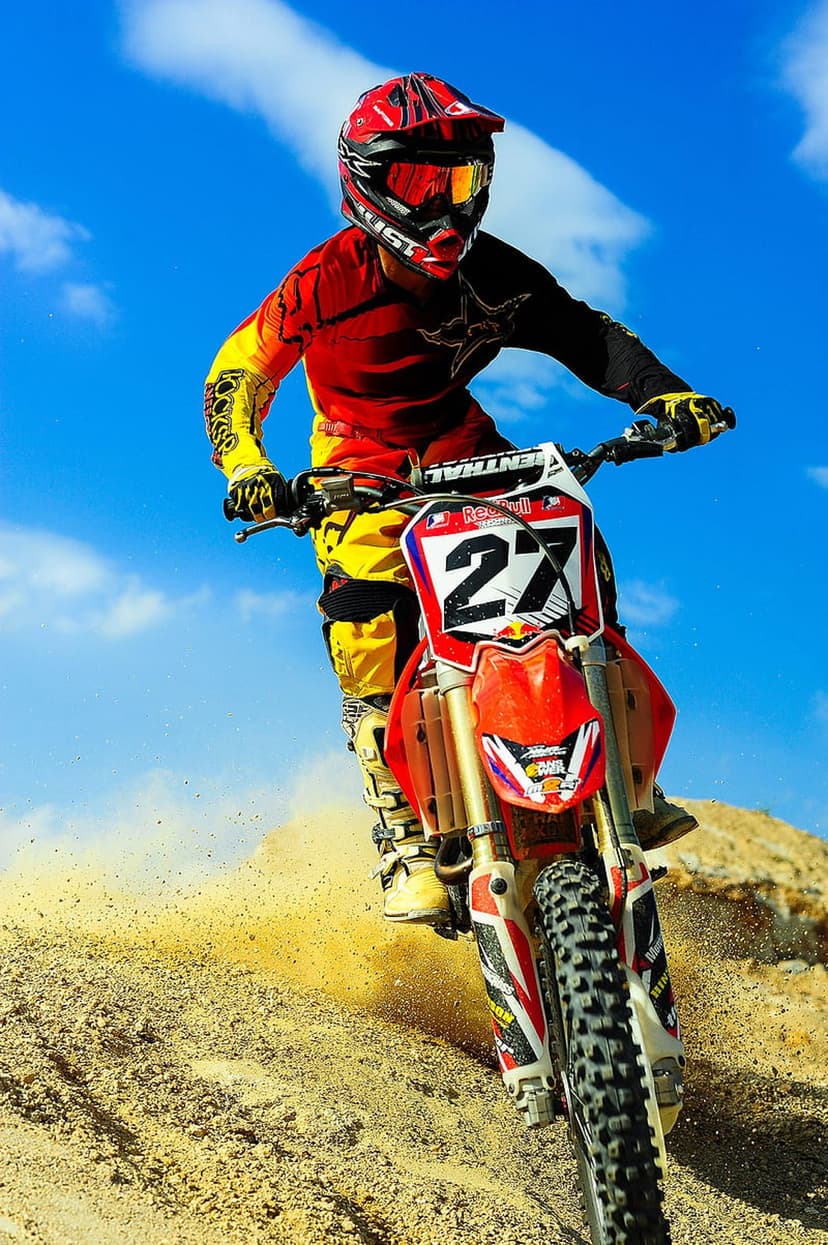 Motocross rider in a red helmet kicks up clouds of dust while racing a dirt bike under a bright blue sky.