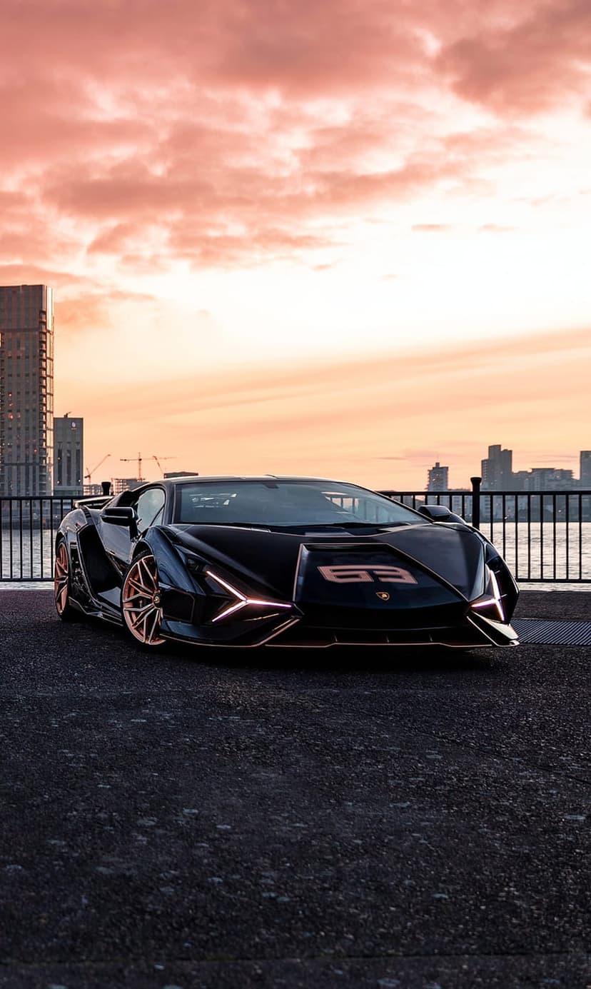 Lamborghini SCV12 with rose gold trim on asphalt before a vibrant sunset skyline with glowing city lights.