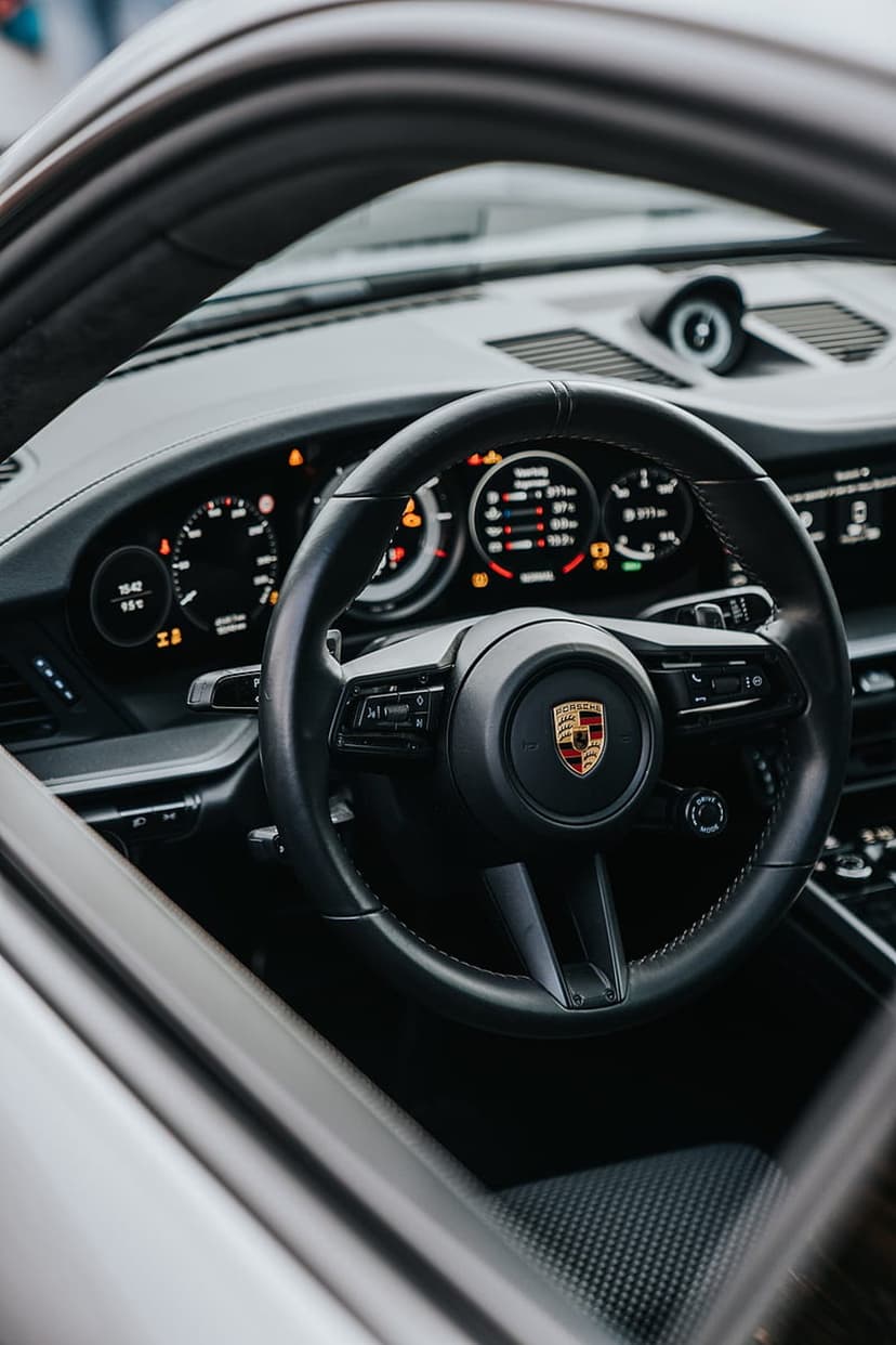 Porsche 911 steering wheel with a gold crest sits before a glowing dashboard display in a luxury car interior.