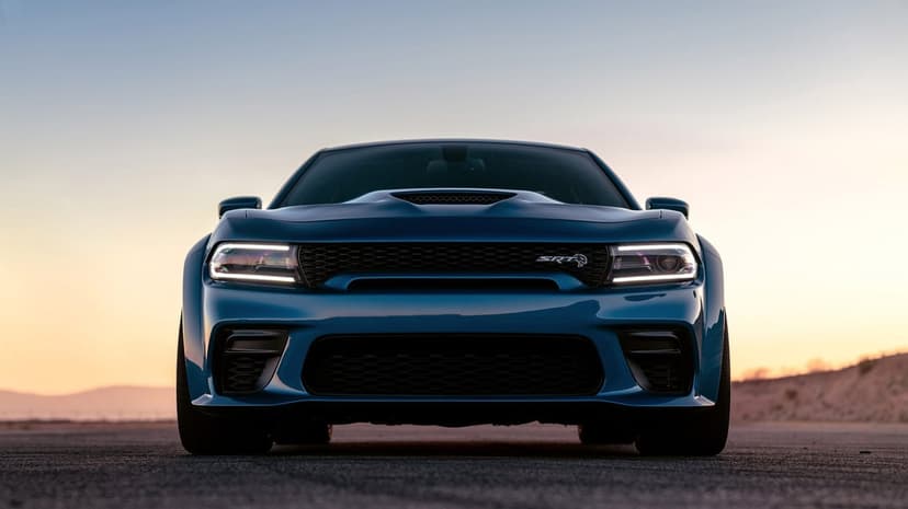 Front view of a blue Dodge Charger SRT Hellcat Widebody on a road at dusk with glowing LED headlights.