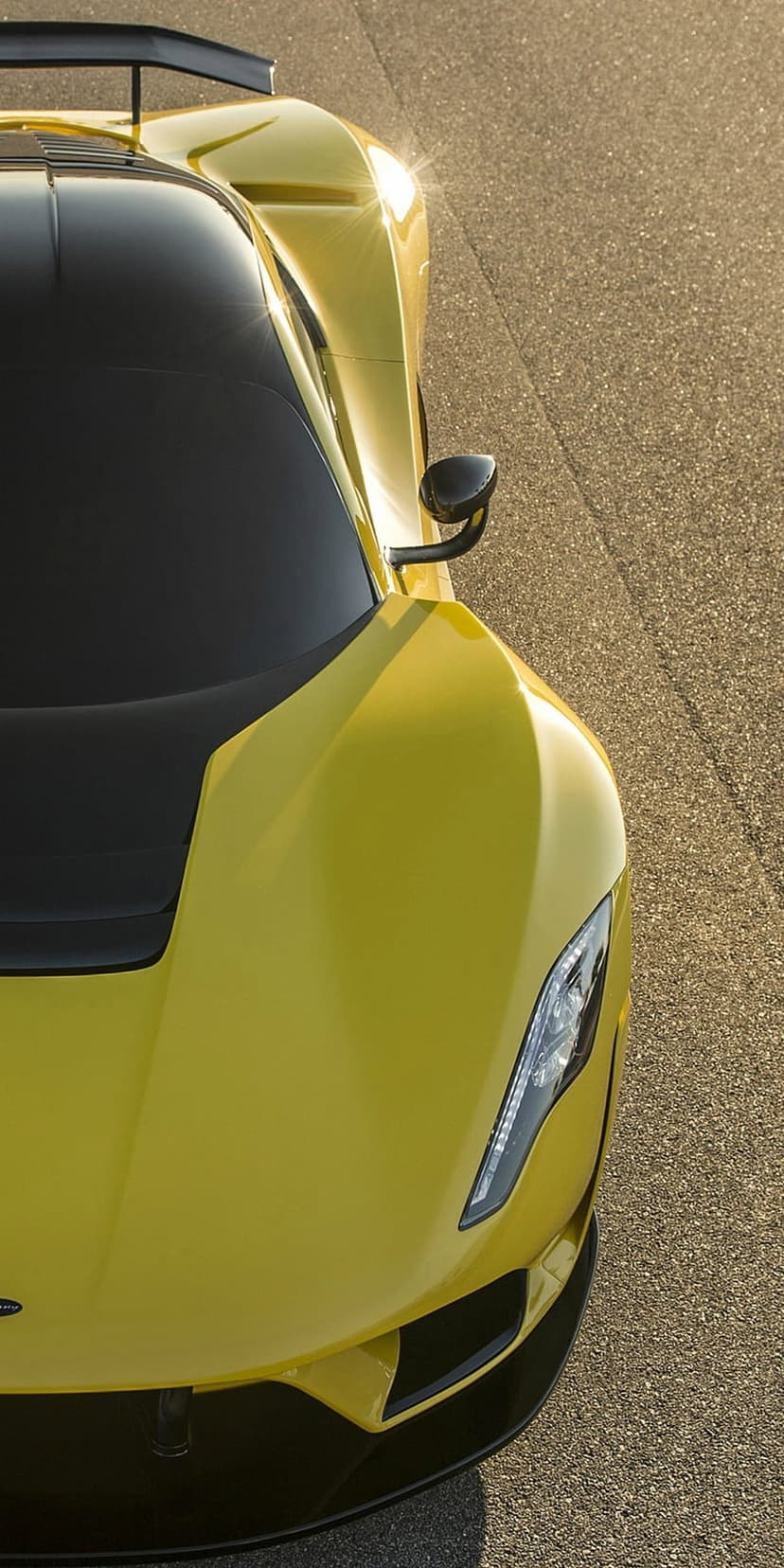 Yellow sports car headlight and spoiler with sunlight reflecting off its polished yellow paint on dark asphalt.