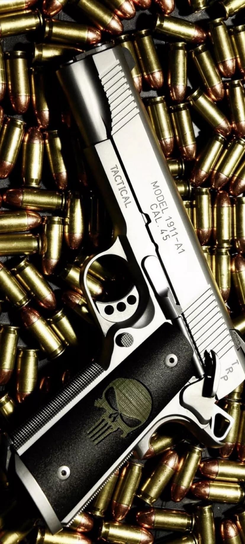 Tactical 1911-A1 pistol with a skull grip lies on brass ammunition shells under focused, dramatic lighting.