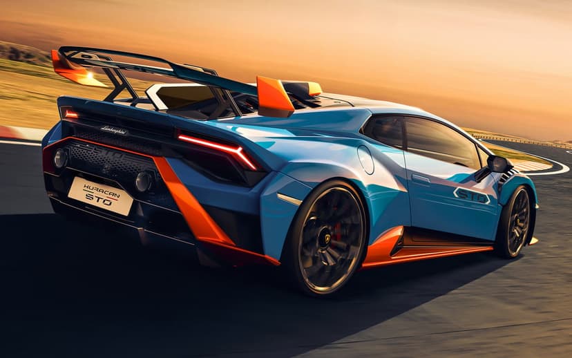 Blue Lamborghini Huracan STO with orange accents speeding on a racetrack during a golden hour sunset.