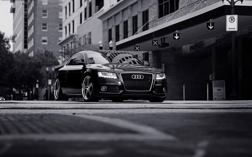 Black Audi coupe parked on an urban street with glowing headlights and custom rims in monochrome.