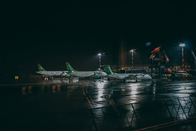 Commercial airplanes parked on a wet tarmac reflecting yellow floodlights against a dark midnight sky.