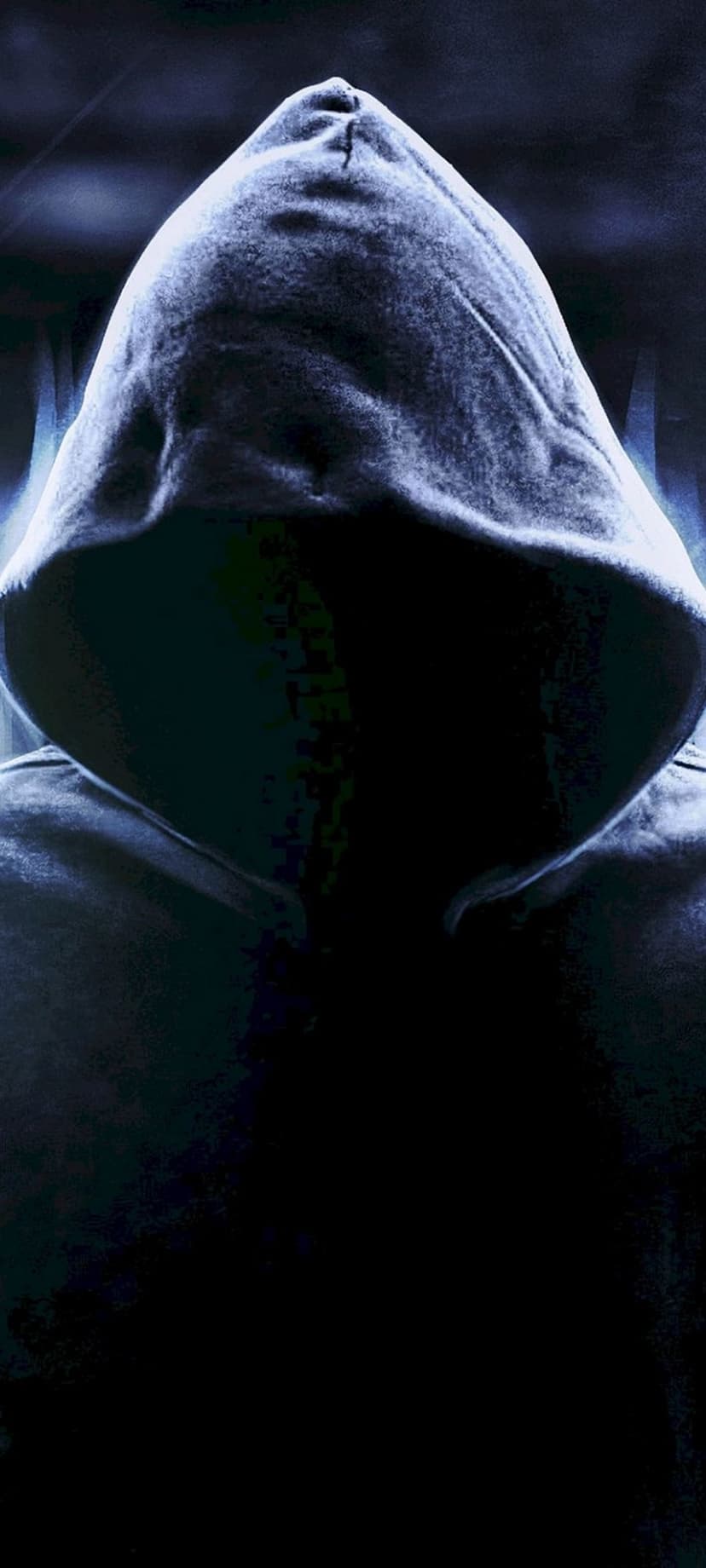 Hooded person stands in deep shadow with cool blue lighting accentuating the fabric folds and obscured face.