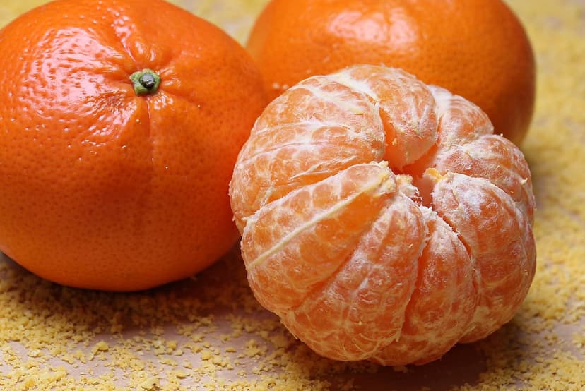 Peeled tangerine segments with white pith in front of two whole citrus fruits on a textured yellow surface.