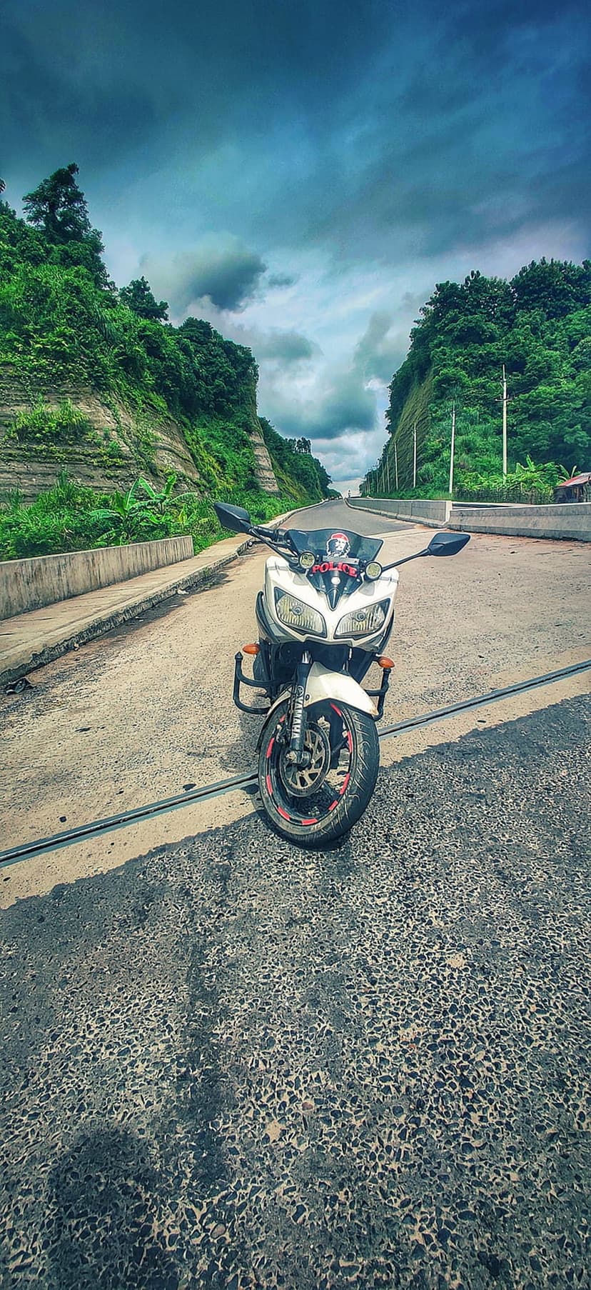 White sports motorcycle parked on an asphalt road between steep green hills under a moody, overcast sky.