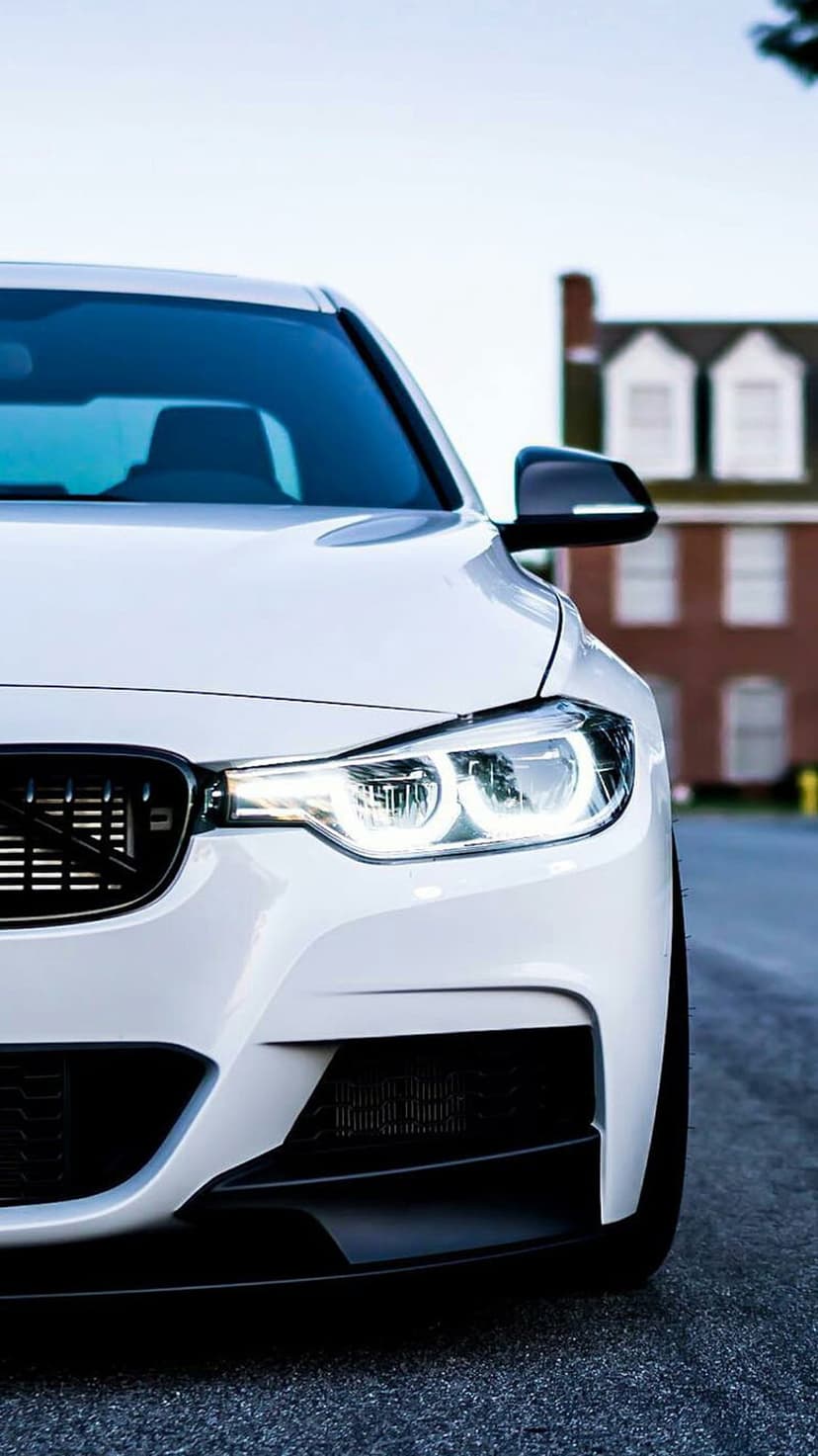 White BMW M Sport front grille and sharp LED headlights against a blurred brick wall in an urban setting.