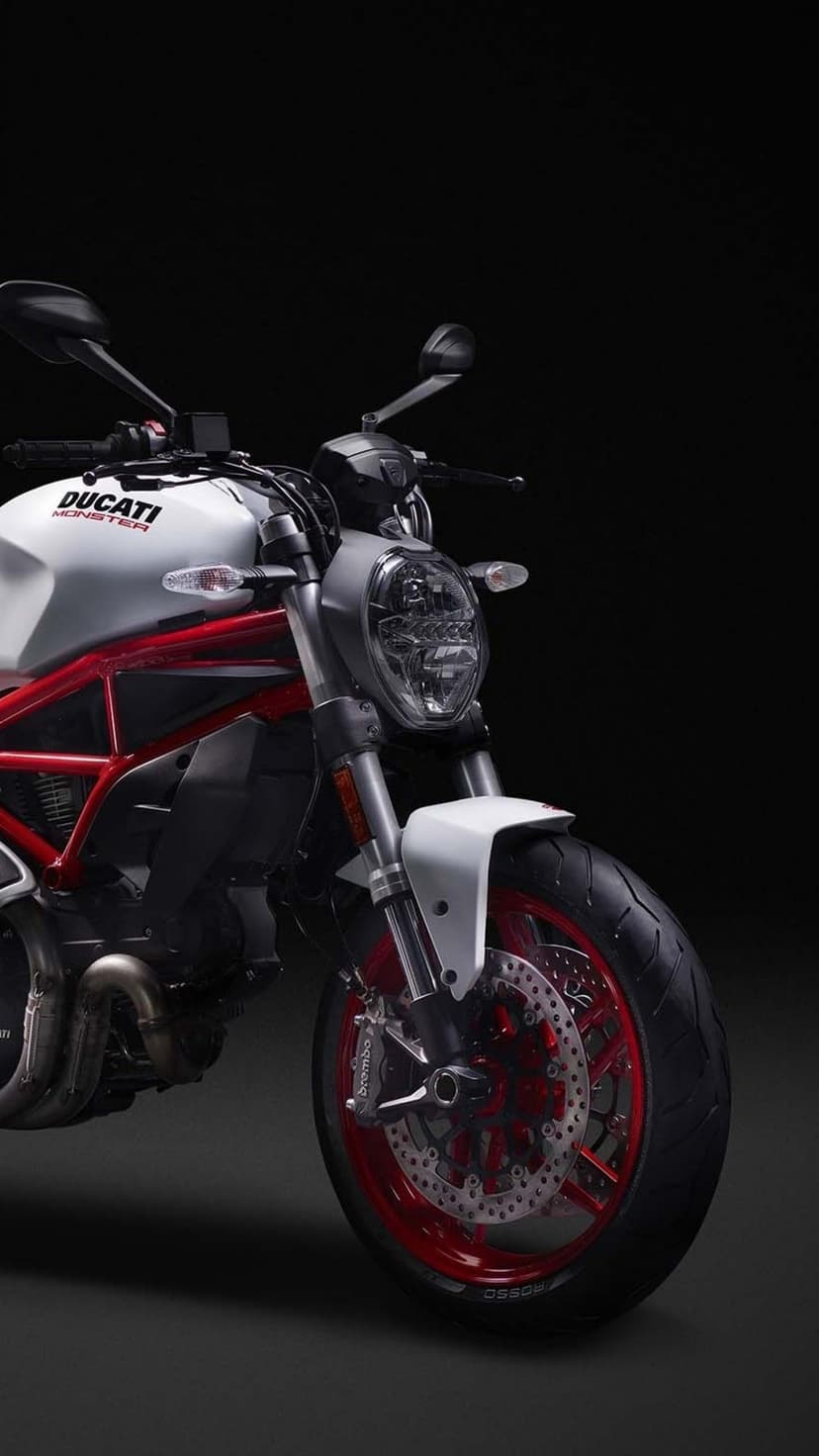 Ducati Monster motorcycle with a white tank and red frame against a dark background in portrait orientation.