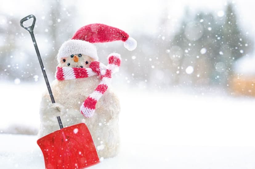 Snowman wearing a Santa hat and red scarf holds a shovel as large snowflakes fall in a blurred winter forest.