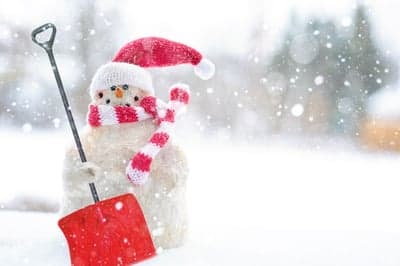 Snowman with red shovel and hat in falling snow