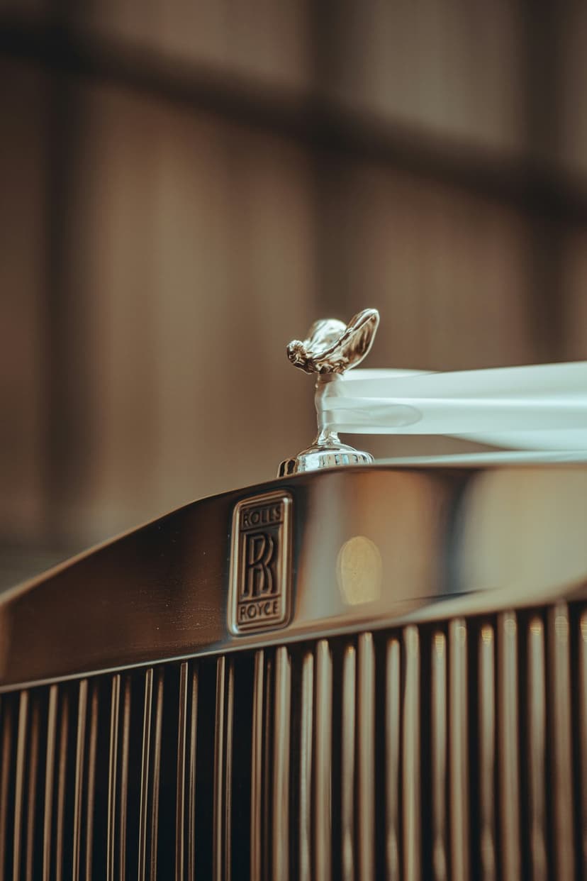 Spirit of Ecstasy ornament stands atop a polished vertical grille with golden light reflecting on chrome surfaces.