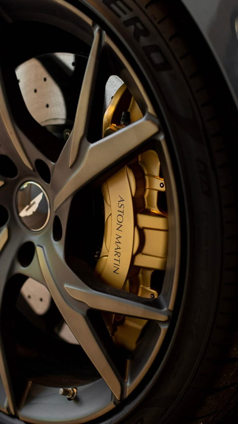 Aston Martin gold brake caliper with black etched branding visible through multi-spoke metallic alloy wheels.