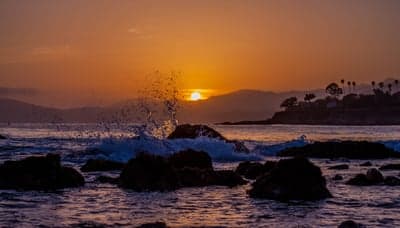 Dramatic Sunset Over Rocky Coastline with Waves Crashing
