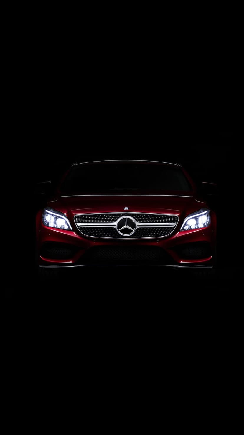 Crimson Mercedes-Benz front grille and illuminated headlights emerge from darkness in a portrait view.