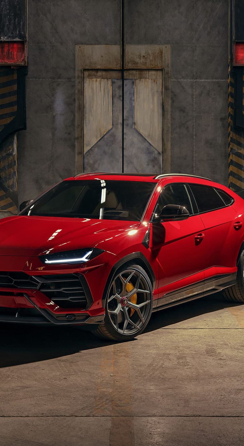 Red Lamborghini Urus SUV parked in a warehouse beside a large metal door with low-key industrial lighting.