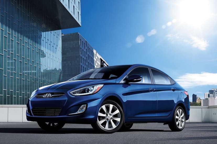 Blue sedan parked on asphalt near a glass building under bright sunlight with a visible lens flare effect.