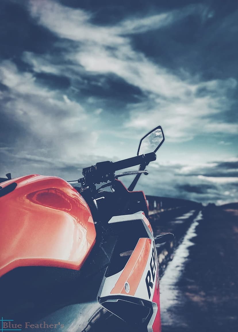 Orange and white sportbike parked on an asphalt roadside under heavy dark storm clouds from a low perspective.