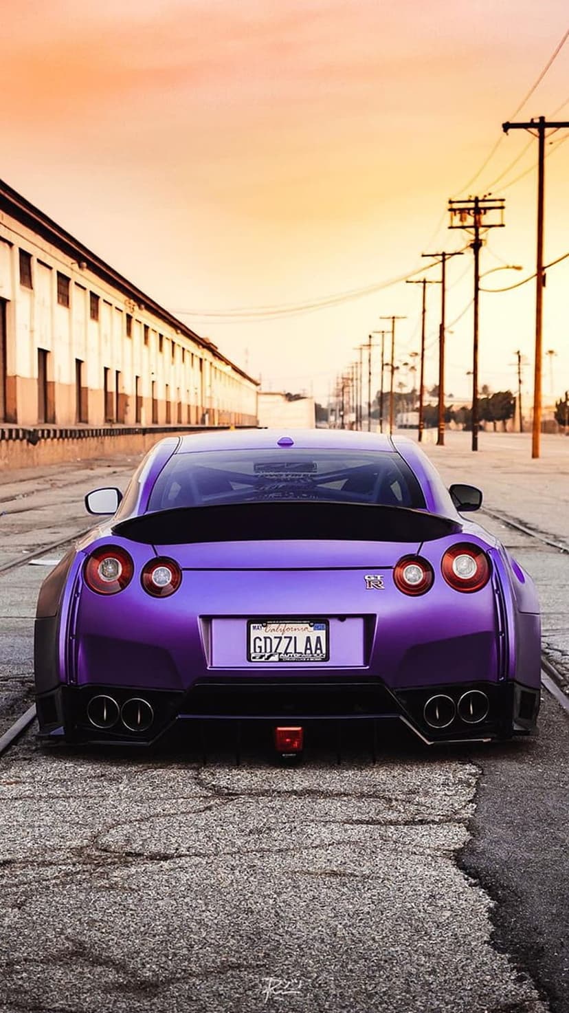 Purple Nissan GT-R rear view with glowing taillights and a large spoiler parked on a street during a golden sunset.