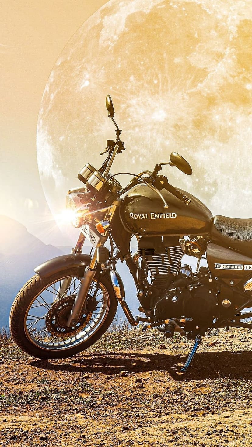 Royal Enfield motorcycle parked on rocky ground with a colossal full moon illuminating the dark night sky.