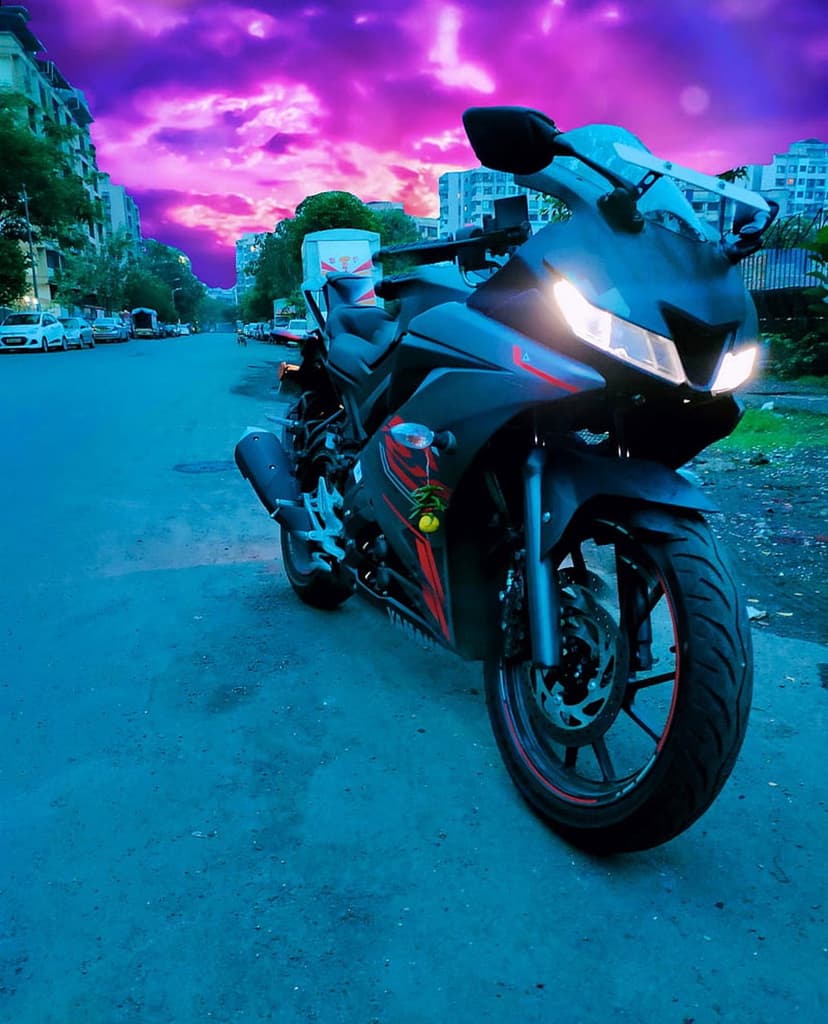 Black sport motorcycle with red accents parked on an asphalt street under a vibrant purple and pink sunset sky.