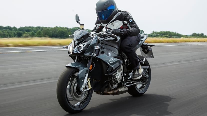 A rider on a grey BMW S1000R motorcycle speeding down a track with motion blur and a blue helmet visor.