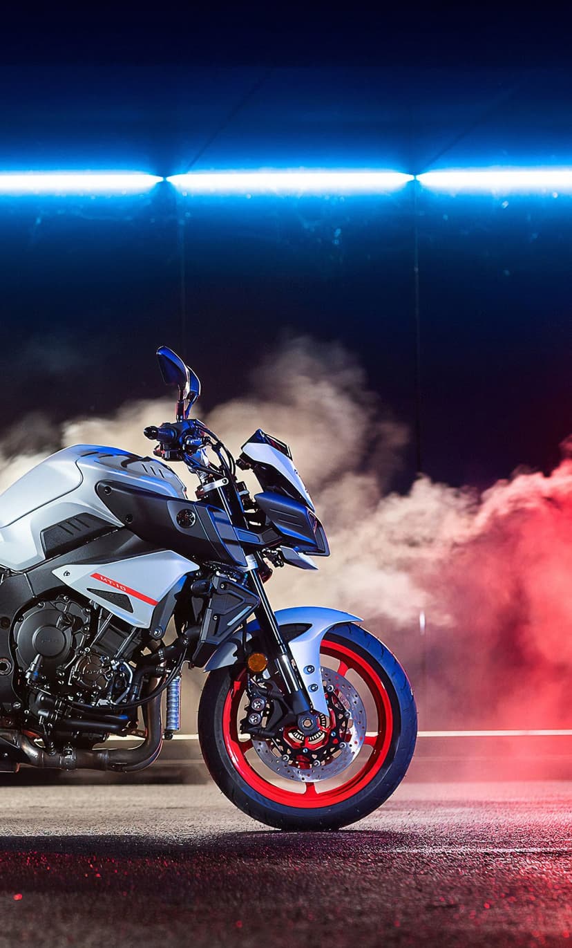 White Yamaha MT-10 motorcycle with red wheels parked in front of red smoke and a blue neon light bar.