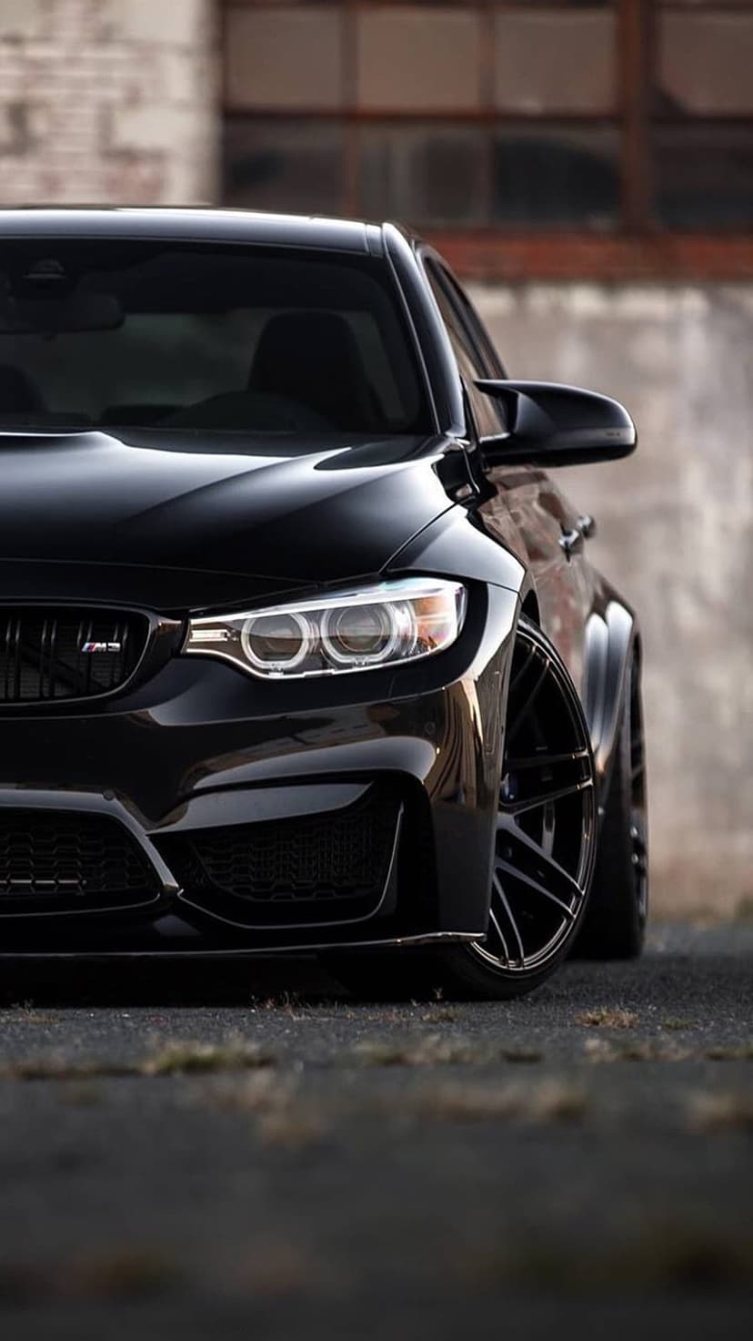BMW M4 Coupe with illuminated LED headlights, black kidney grille, and alloy wheels against a brick wall.