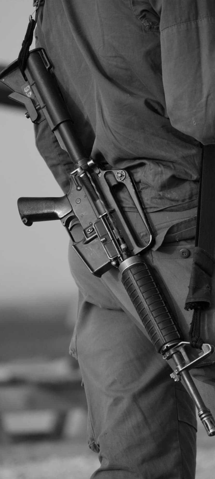 Soldier wearing camo fatigues with a tactical rifle slung across their back in a close-up grayscale view.