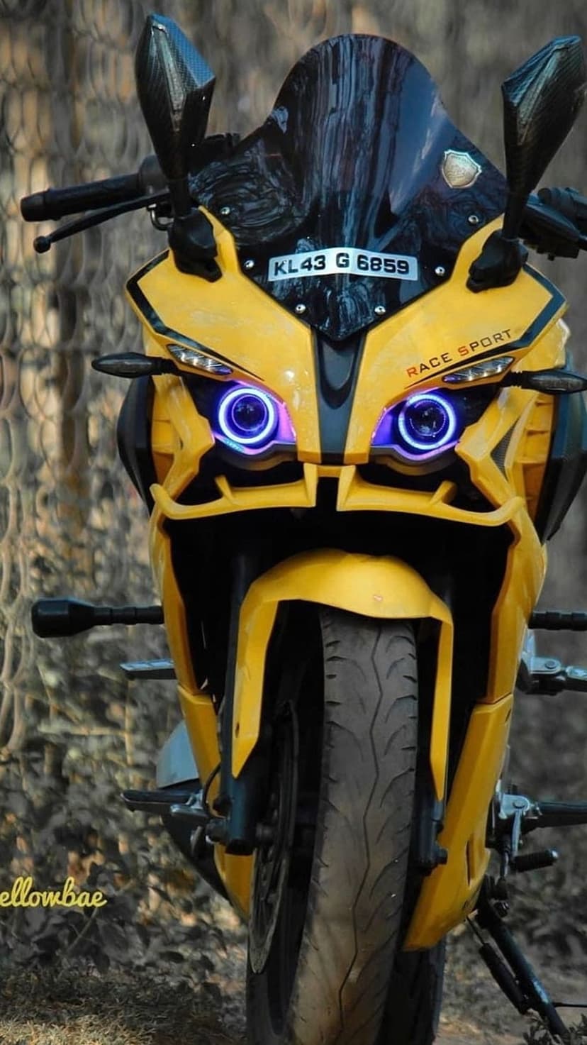 Yellow sport motorcycle with glowing blue halo headlights, a black windshield, and carbon fiber mirror details.