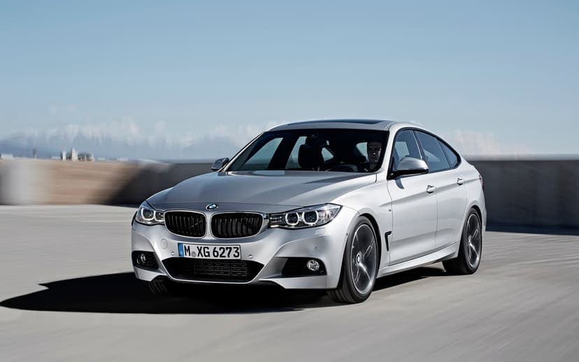 Silver BMW 3 Series Gran Turismo luxury sedan driving on a coastal road under a clear blue sky with motion blur.