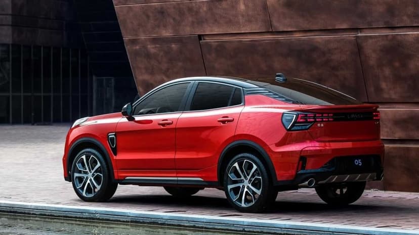 Side view of a red crossover SUV parked beside a modern bronze building near a reflective water pool.