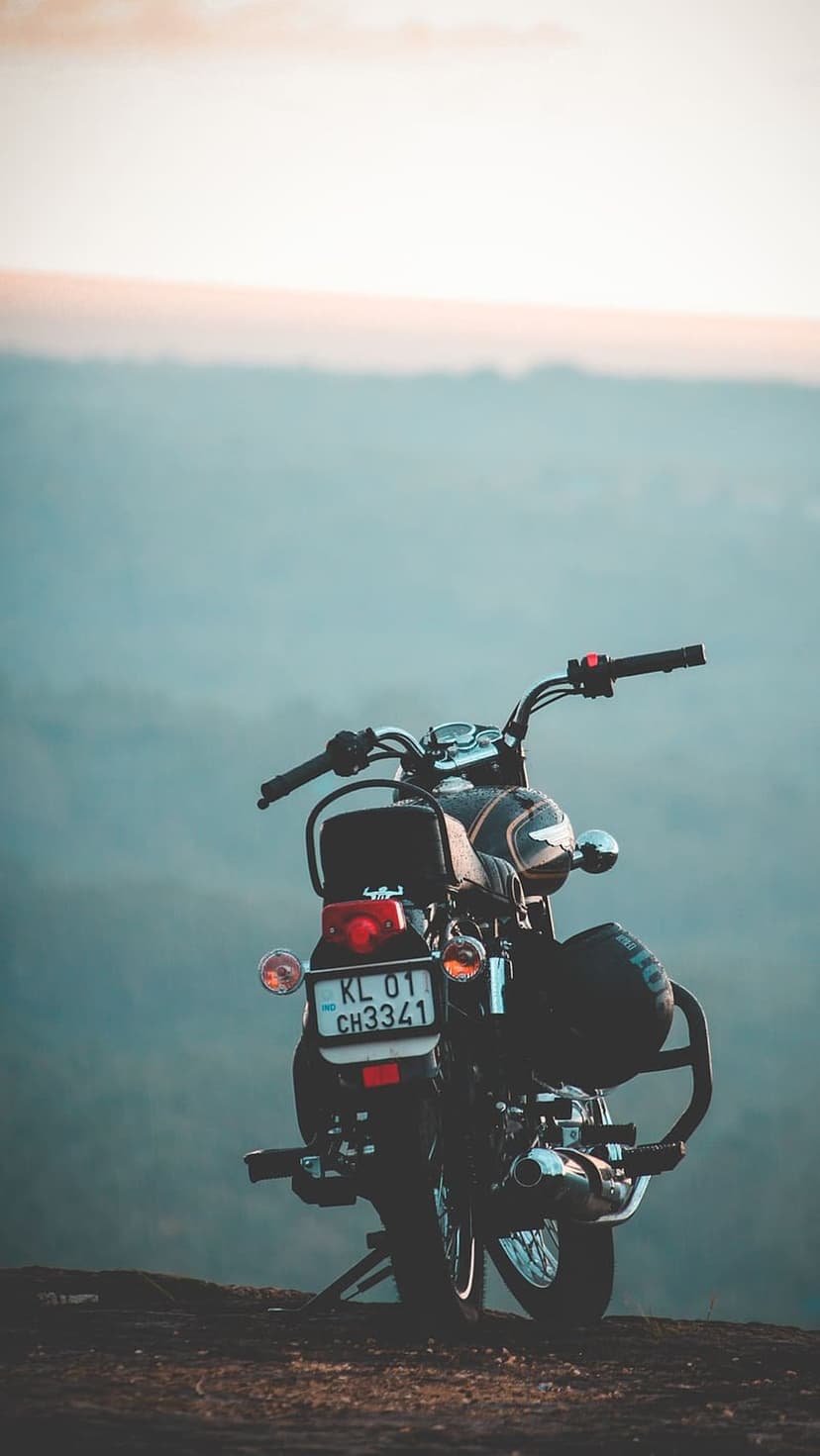 Classic motorcycle on a rocky cliff overlooking a misty mountain valley under a vibrant orange sunset sky.
