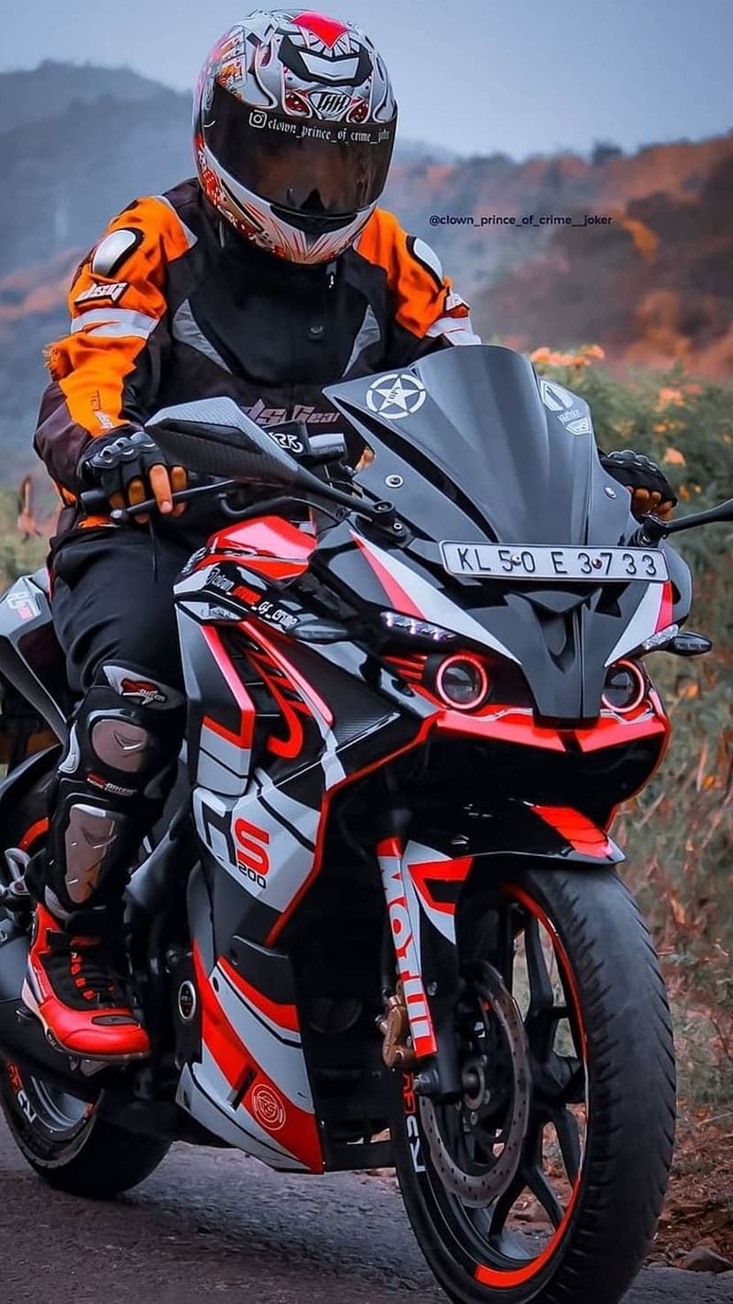 Motorcyclist in orange gear on a red sportbike sits against a blurred green forest backdrop on a country road.