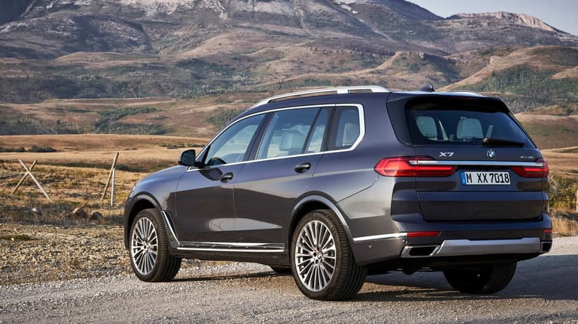 Dark grey BMW X7 SUV parked on a gravel path against a backdrop of rugged mountains and dry hillsides.