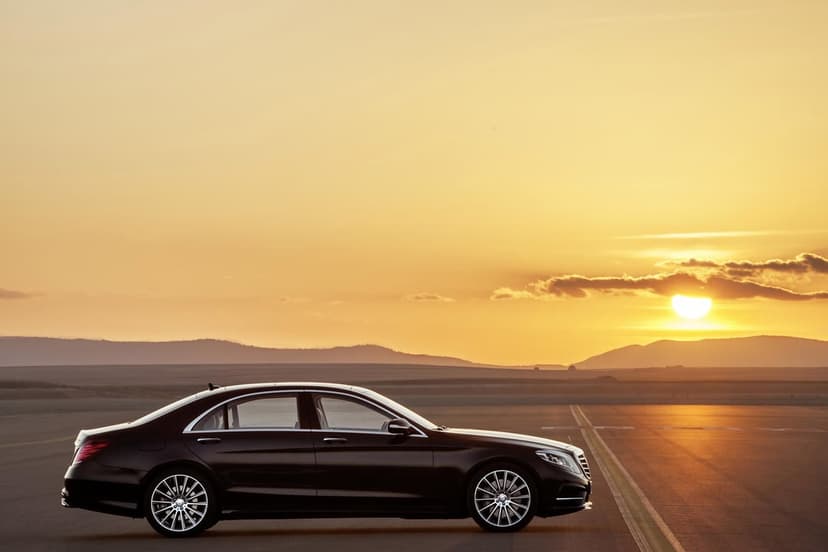 Side profile of a black Mercedes-Benz S-Class on a flat runway under a glowing golden sunset sky.